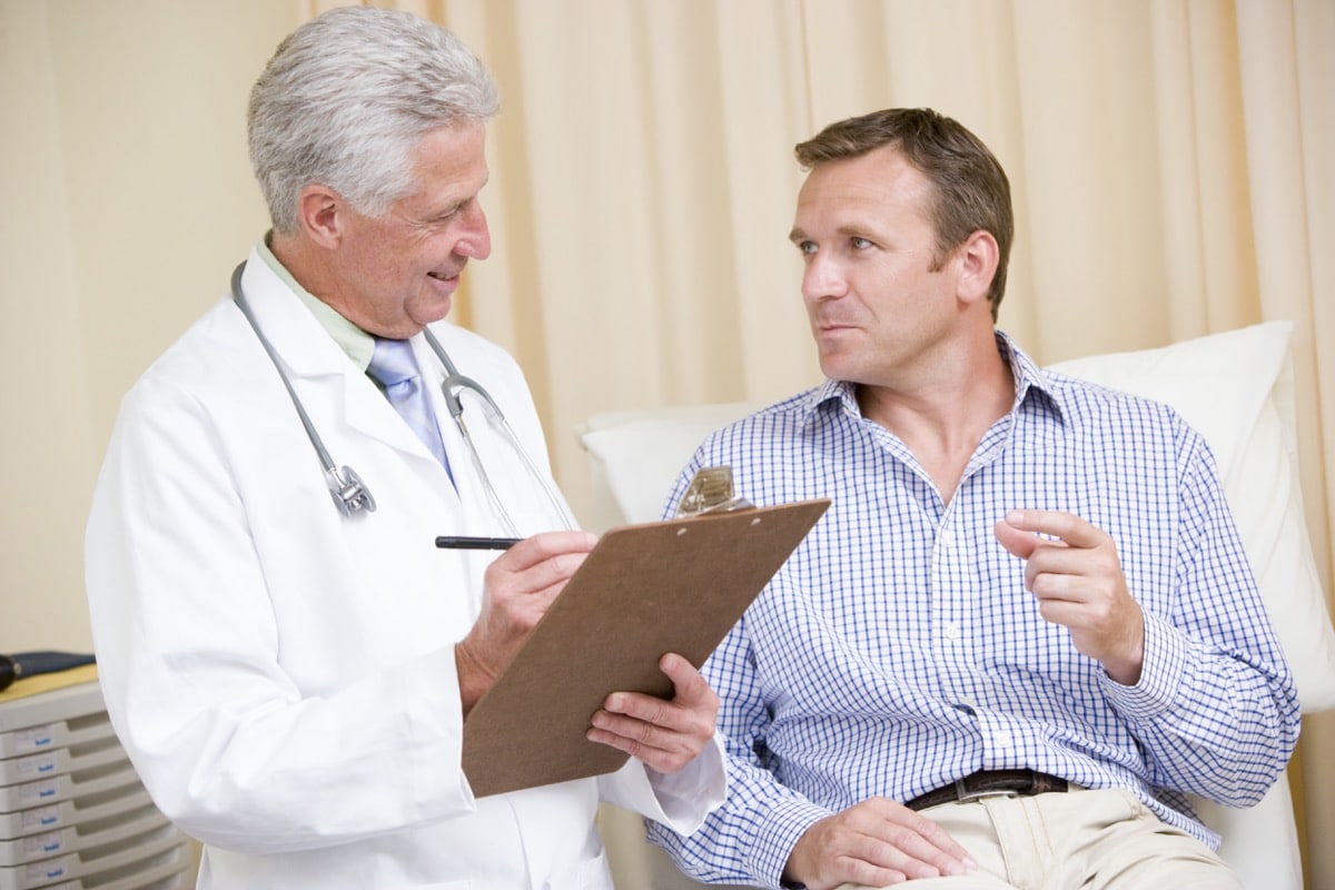 Doctor writing on clipboard while giving man checkup in exam room